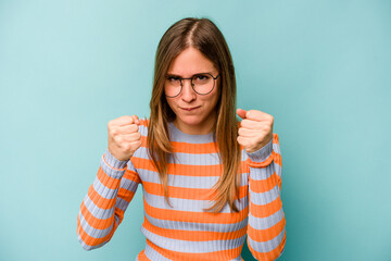 Young caucasian woman isolated on blue background showing fist to camera, aggressive facial expression.