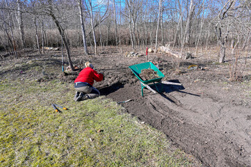 woman on her knees clears weeds in spring