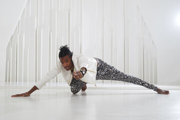 A black guy in stage clothes is dancing in a bright room.