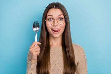 Photo of excited funny lady hold spoon protrude tongue lick lip wear specs beige sweater isolated blue color background