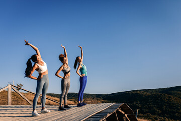 Group of sporty female friends stretching before running outdoors.
