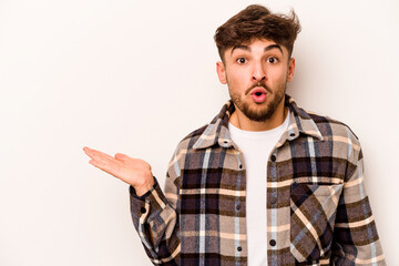 Young hispanic man isolated on white background impressed holding copy space on palm.