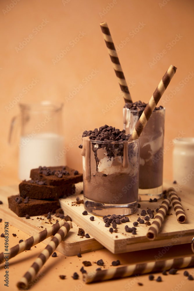 Sticker Vertical shot of a chocolate milkshake in the glass next to some chocolate chips and sweets.