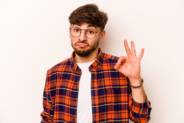 Fototapeta premium Young hispanic man isolated on white background winks an eye and holds an okay gesture with hand.
