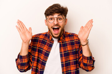 Naklejka premium Young hispanic man isolated on white background receiving a pleasant surprise, excited and raising hands.