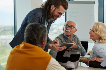 Obraz premium Young hipster educator teaching group of senior multiracial people using technology and the internet in the classroom.