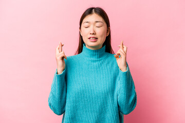 Young Chinese woman isolated on pink background crossing fingers for having luck