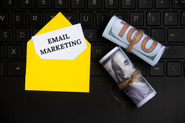 Top view of email marketing text on notepad in an envelope with bank notes and laptop background.
