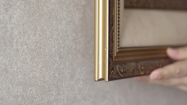 women's hands hang a picture on the wall. baguette. finishing material for the manufacture of frames for paintings or mirrors, interior design, room walls, ceilings. services of an artist designer