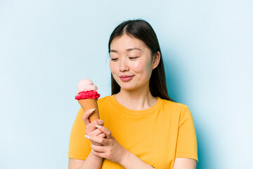Young asian woman eating an ice cream isolated on blue background