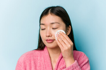 Young asian woman holding a facial disk isolated on pink background