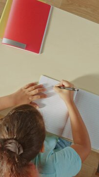 Zoom Out Top View Camera: Little Girl in School, Writing in Her Exercise Notebook. Video Footage with Vertical Screen Orientation 9:24