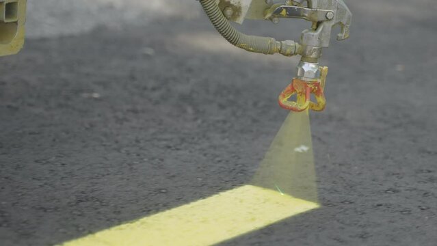 Close up, road marking machine nozzle spraying yellow paint onto asphalt