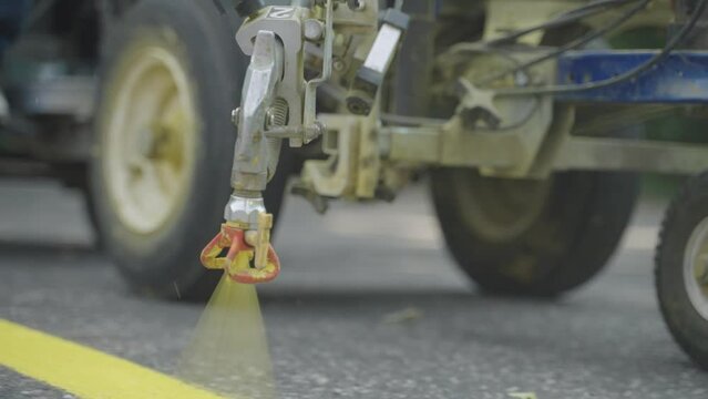 Close up, road marking machine spraying yellow paint through nozzle on asphalt