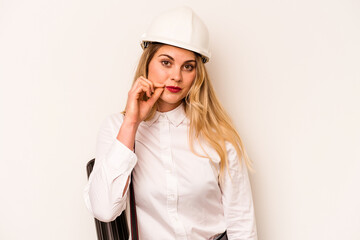 Young architect woman with helmet and holding blueprints isolated on white background with fingers on lips keeping a secret.