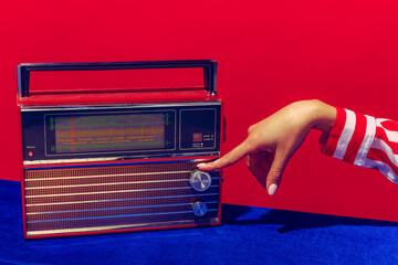 Retro radio. Female hand holding, touching radioreceiver isolated on blue and red background. Vintage, retro fashion style. Pop art photography.