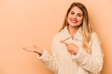 Young caucasian woman isolated on beige background excited holding a copy space on palm.