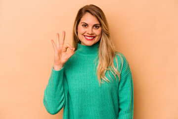 Young caucasian woman isolated on beige background cheerful and confident showing ok gesture.