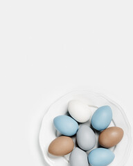 Painted Easter eggs blue, gray, beige colored on round white plate, light background with copy space. Chicken egg pastel shades. Easter holiday food, simple minimal design aesthetic flat lay