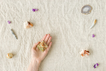 Top view crystal and stone on table, female hand hold one of healing minerals agate, quartz, amethyst, onyx. Stones for crystal therapy. Flat lay semiprecious gems, alternative medicine