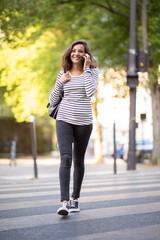 Full body smiling young woman walking and talking with mobile phone
