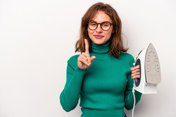 Young caucasian woman holding iron isolated on white background showing number one with finger.