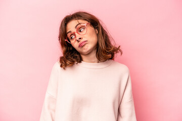 Young caucasian woman isolated on pink background shrugs shoulders and open eyes confused.