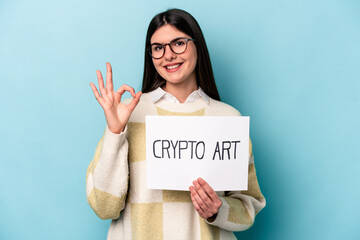 Fototapeta na wymiar Young caucasian business woman holding a crypto art placard isolated on blue background cheerful and confident showing ok gesture.