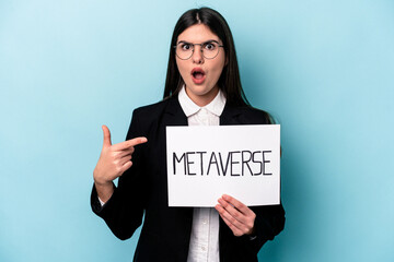 Young caucasian business woman holding a metaverse placard isolated on blue background pointing to the side