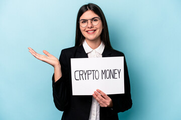 Young caucasian business woman holding a crypto money placard isolated on blue background showing a copy space on a palm and holding another hand on waist.