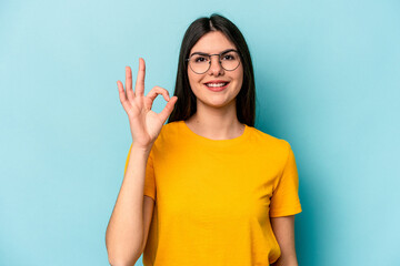 Young caucasian woman isolated on blue background cheerful and confident showing ok gesture.