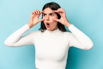 Young caucasian woman isolated on blue background keeping eyes opened to find a success opportunity.