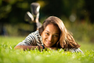 Front of beautiful young woman lying on grass in park and smiling
