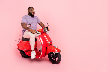 Photo of funny excited guy dressed violet t-shirt driving moped empty space isolated pink color...