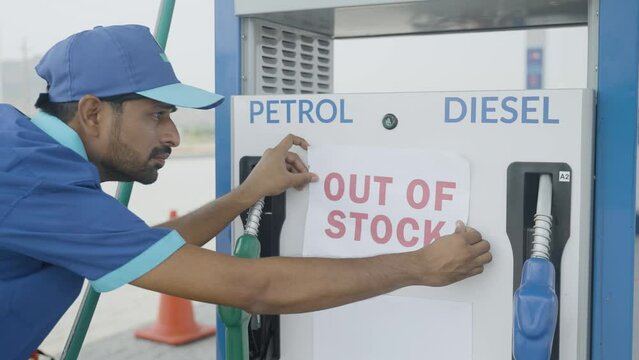 Worker at petrol or gas filling sation pasting out of stock notice sign board - concept of economy and fuel crisis shortage.