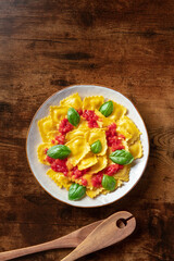 Ravioli with tomato sauce and fresh basil leaves, overhead shot. Italian recipe on a rustic wooden table