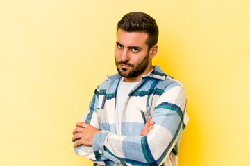 Young caucasian man isolated on yellow background frowning face in displeasure, keeps arms folded.
