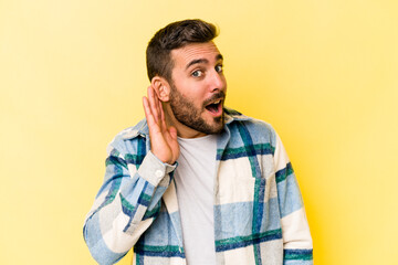 Obraz premium Young caucasian man isolated on yellow background trying to listening a gossip.
