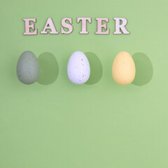Three Easter eggs of different colors with a stronger shade and the inscription Easter made of wood on a light green background with copy space. Minimal holiday composition.
