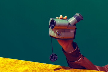 Concept of pop art photography. Using retro gadgets. Human hand holding videocamera isolated on green-yellow background. Vintage fashion style. Concept of nostalgia