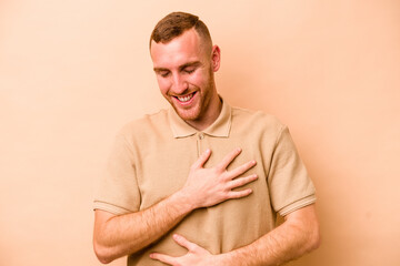 Young caucasian man isolated on beige background laughs happily and has fun keeping hands on...