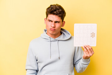 Young caucasian man holding puzzle isolated on yellow background confused, feels doubtful and unsure.