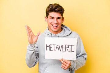 Young caucasian man holding metaverse placard isolated on yellow background receiving a pleasant surprise, excited and raising hands.