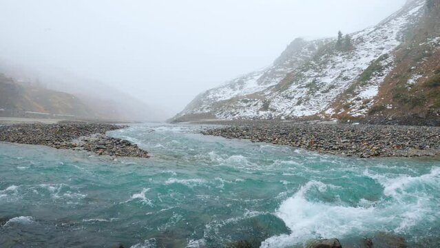 4K shot of Chenab River flowing during the snowfall in the mountains at Sissu in Himachal Pradesh, India. View of blue coloured river during the snowfall after crossing the Atal Tunnel.	
