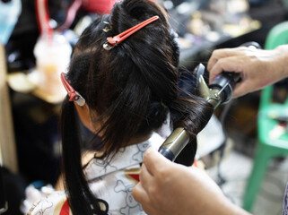 Back view of female hairdresser curling female hair with curling iron in hair salon