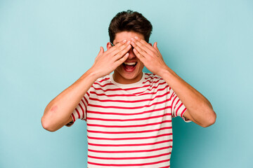 Young caucasian man isolated on blue background covers eyes with hands, smiles broadly waiting for a surprise.