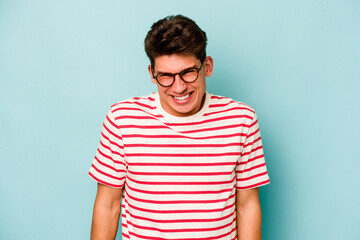 Young caucasian man isolated on blue background laughs and closes eyes, feels relaxed and happy.