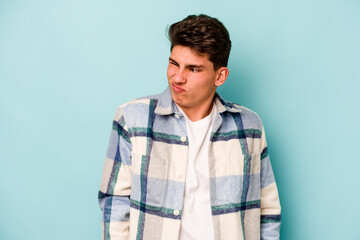 Young caucasian man isolated on blue background shrugs shoulders and open eyes confused.