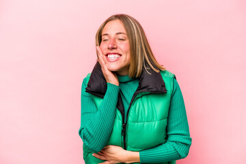 Young caucasian woman isolated on pink background laughs happily and has fun keeping hands on stomach.