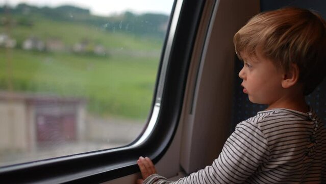 Child staring out train window looking at landscape pass by